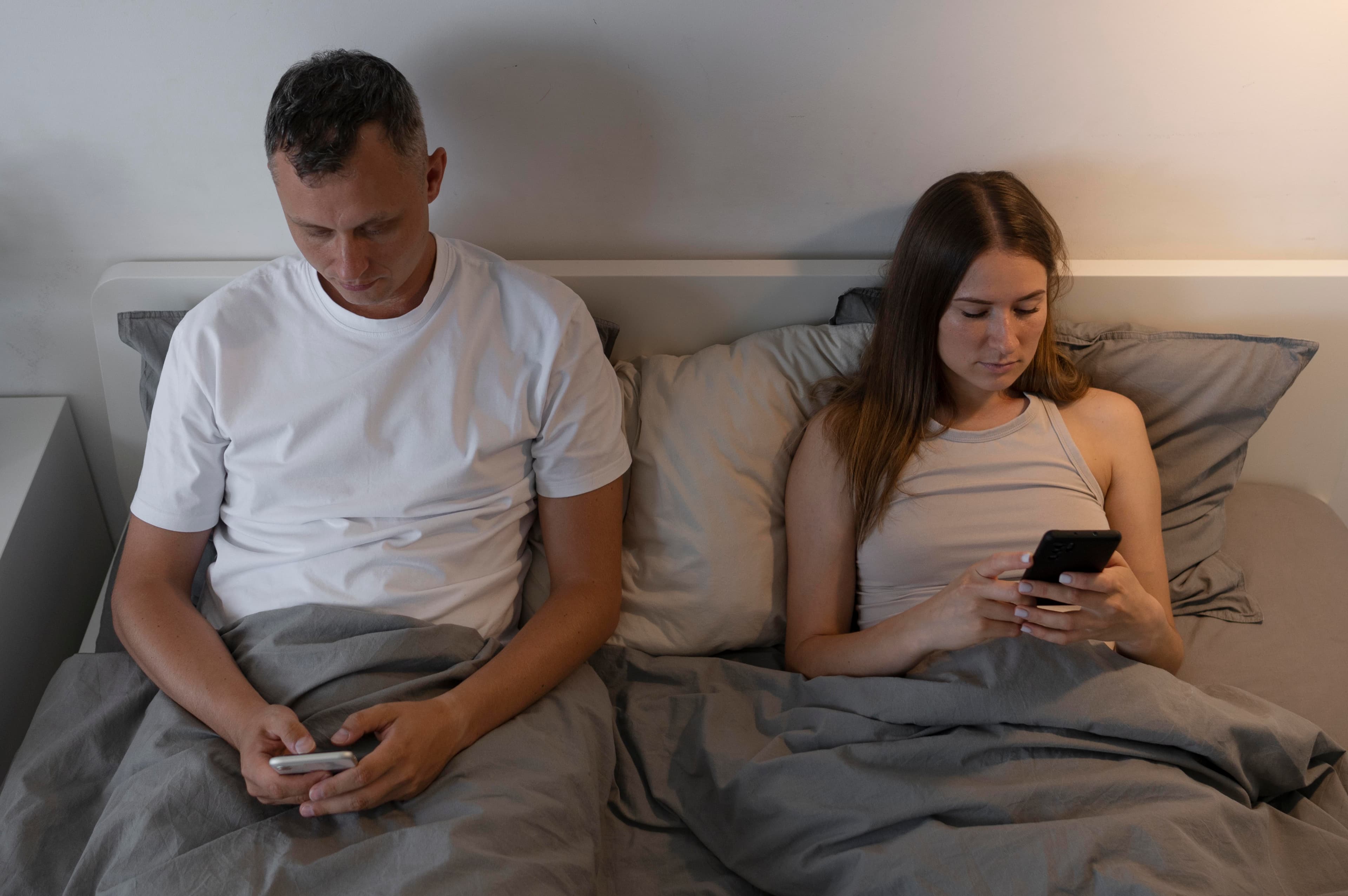 A couple in bed on their phones, disconnected from each other