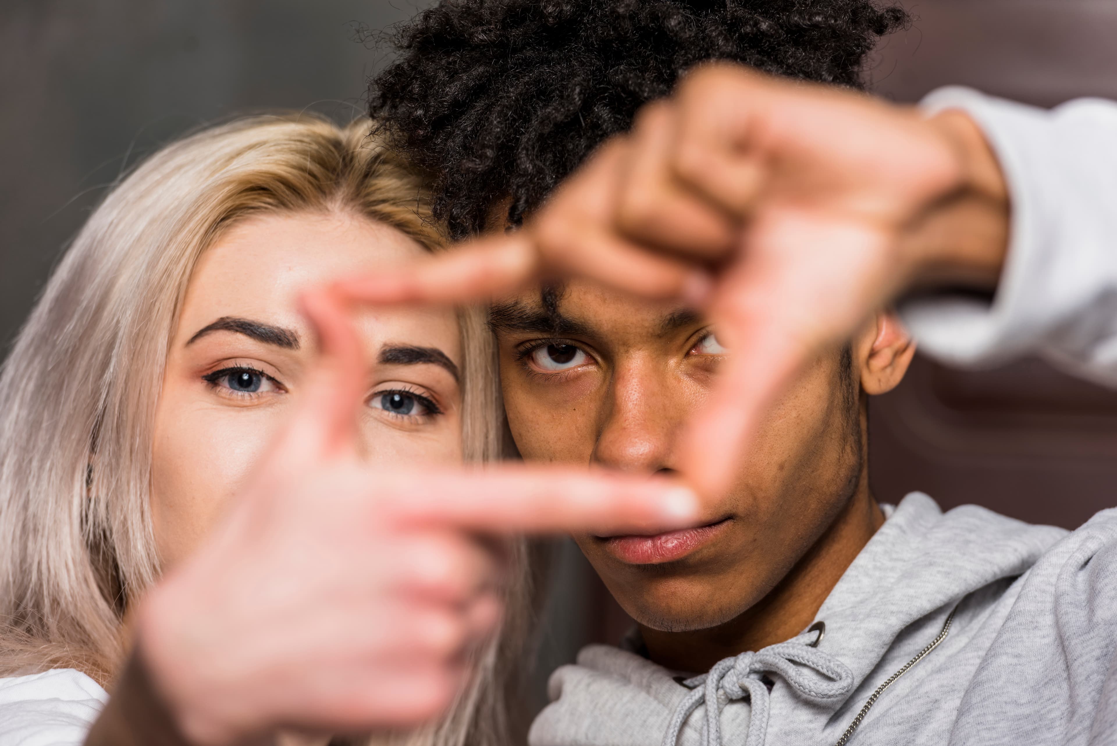 A couple close together, making a frame with their hands as they look at each other